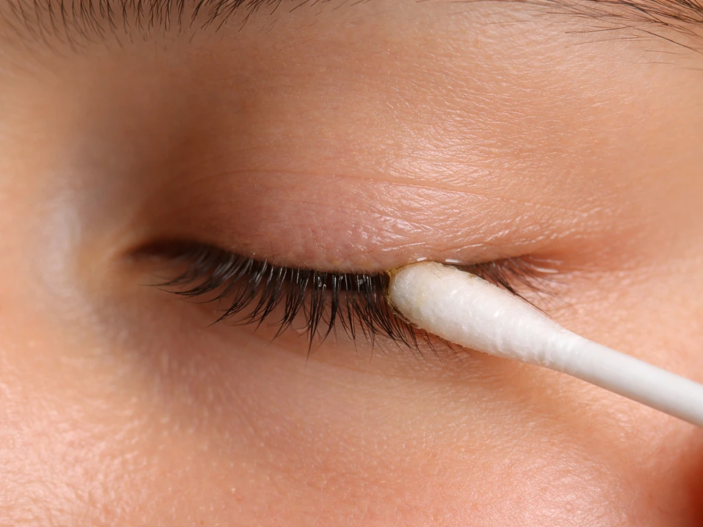 Close-up of an anonymous lash line as castor oil is applied with a cotton swab.