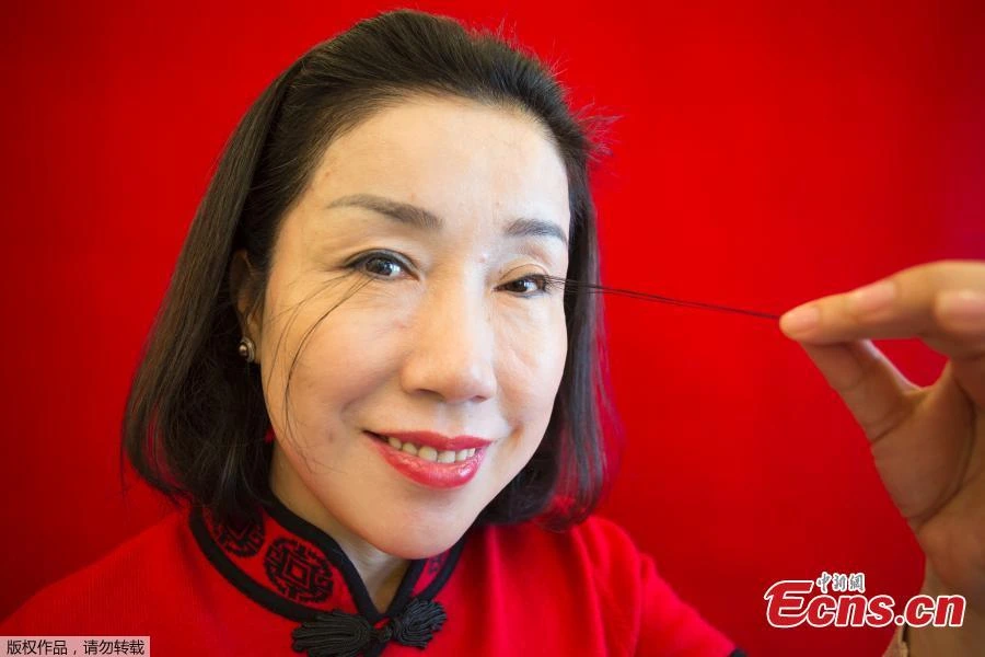 You Jianxia smiling in a red outfit while a hand lifts one of her extremely long eyelashes against a bright red backgrou